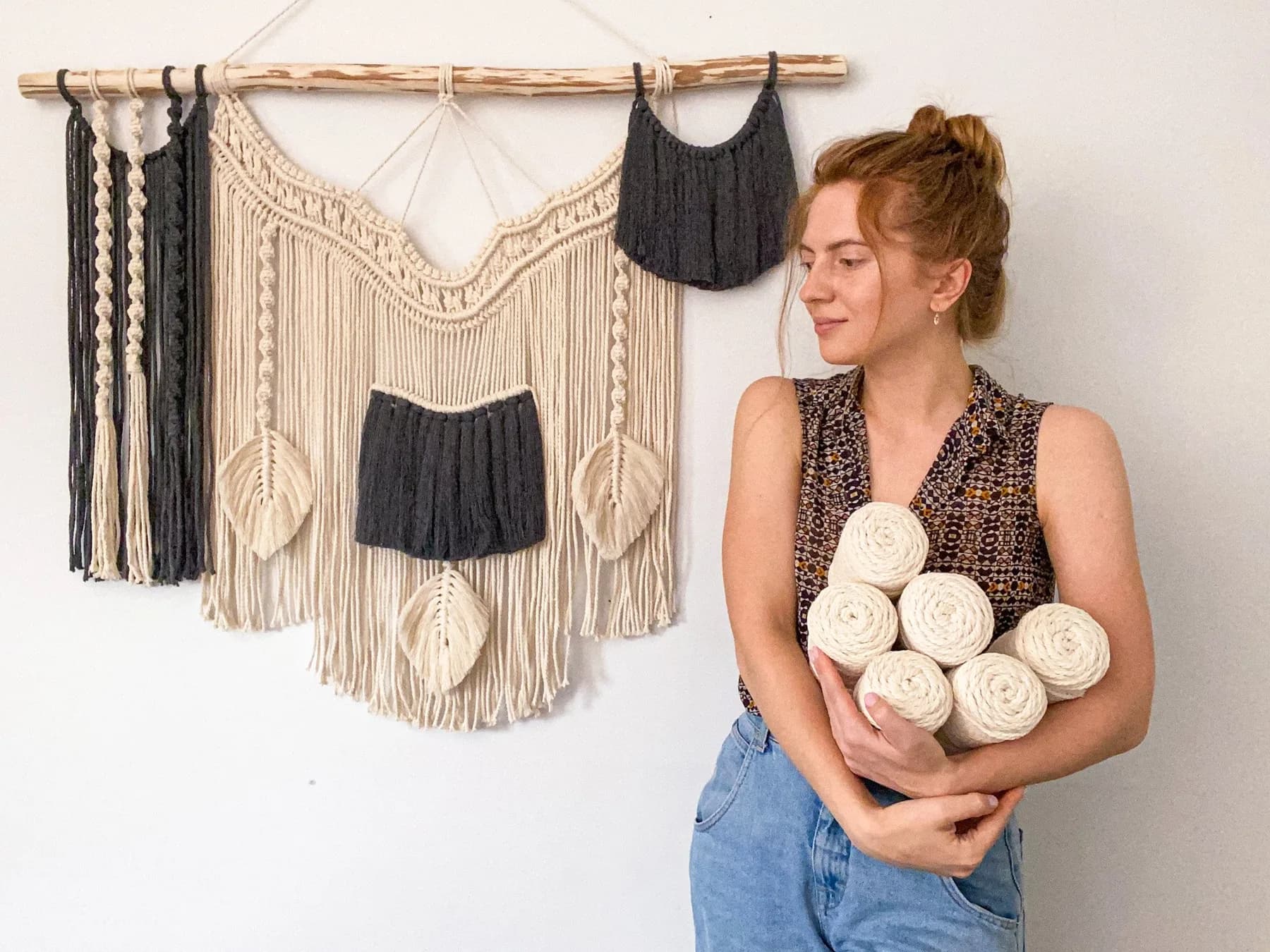 Macramé artist holding spools of cotton cord beside her wall hangings