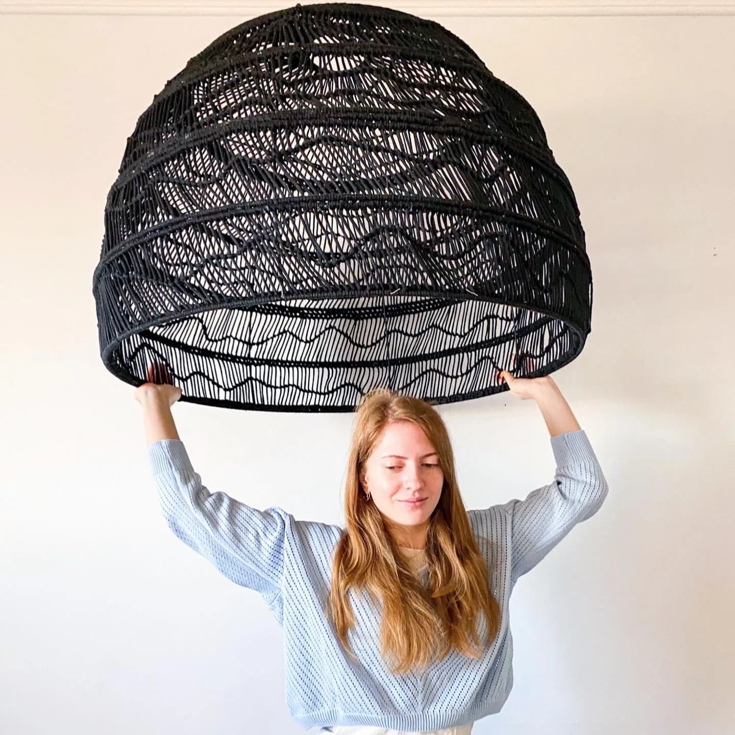 Macramé artist holding a large black knotted lampshade above her head
