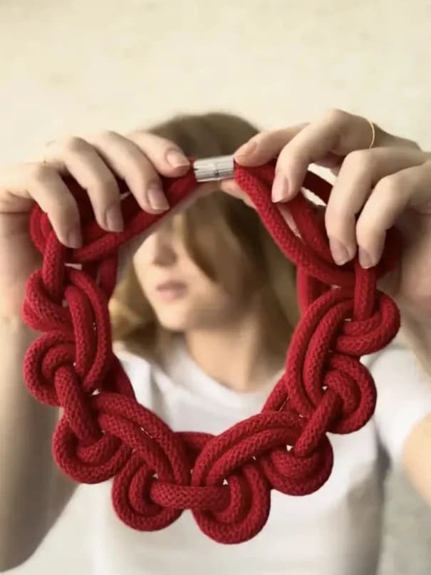 Hands holding a sculptural red knotted necklace