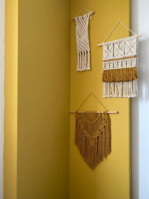 Three knotted wall hangings against an ochre wall